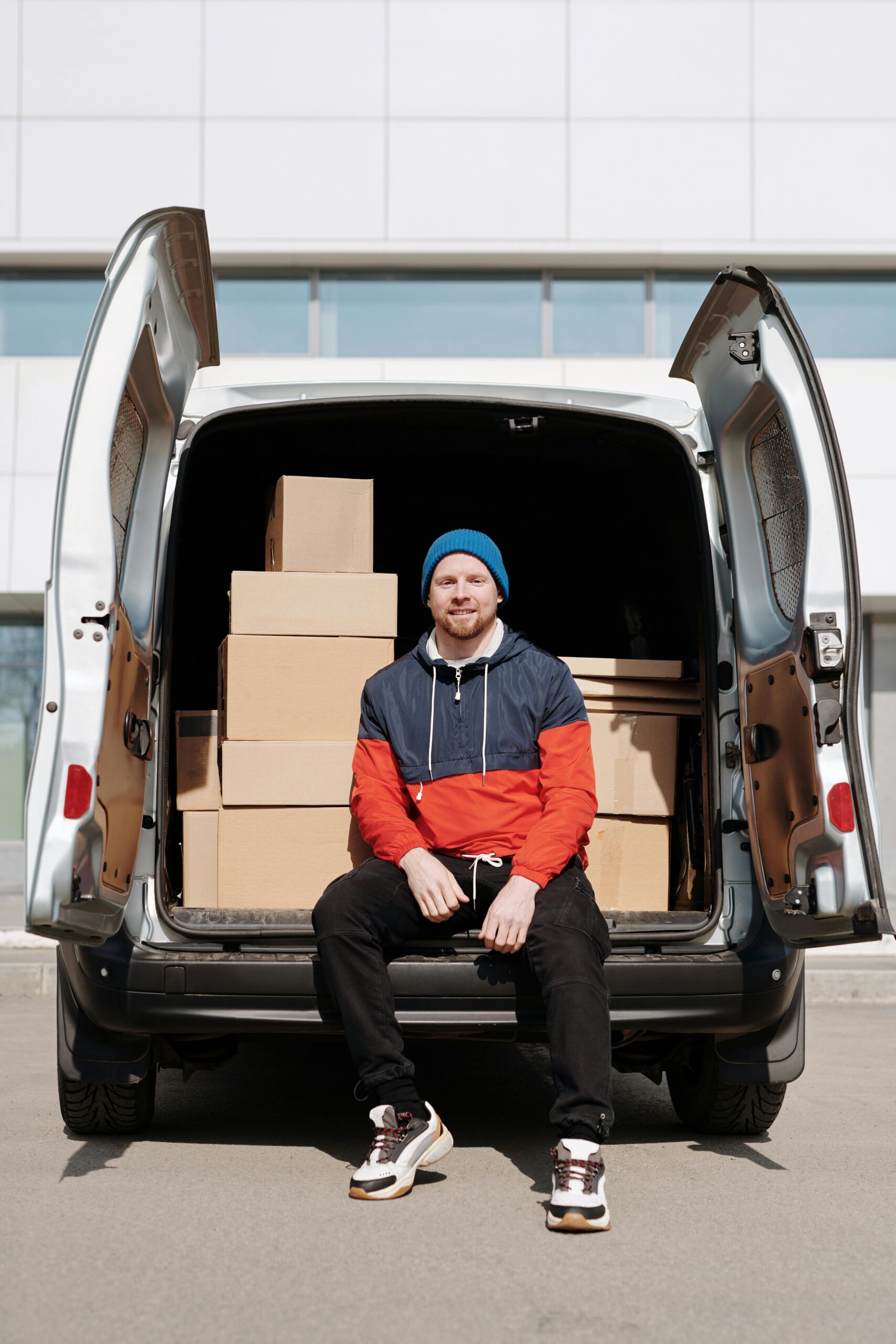 pexels-photo-4391630-4391630 Man in a beanie and jacket sitting on a van tailgate surrounded by cardboard boxes.