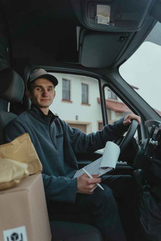 pexels-photo-6169856-6169856 A delivery driver holding documents sits in a van, ready with packages for delivery.